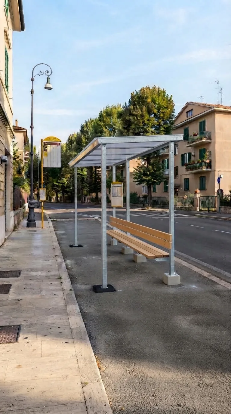 Immagine statica per Flow Veo, YouTube Shorts verticale 9:16, da usare per un timelapse di costruzione. Slargo asfaltato di un quartiere residenziale di pianura italiano, visto in prospettiva obliqua statica a livello d’uomo da circa 18 metri, inquadratura verticale centrata sulla fascia di attesa tra il marciapiede in lastre di pietra chiara in primo piano a sinistra e la corsia stradale a due sensi a destra. Sul fondo tre palazzine basse intonacate color sabbia con persiane verdi; un filare di tigli adulti allinea il lato opposto della strada; un lampione esistente in ghisa scura resta sul bordo del marciapiede; una palina segnaletica gialla già piantata marca la fermata. L’asfalto dello slargo è liscio, grigio scuro, con una fascia di ghiaia fine verso il filare. Luce pomeridiana laterale da sinistra, cielo azzurro con nubi sottili, color grading naturale leggermente caldo. Nessun movimento di camera. Al centro dello slargo, allineata al marciapiede e alla palina gialla, la pensilina autobus è completa e interamente visibile con spazio libero attorno: volume 6 metri di lunghezza, 2,4 metri di profondità e 3 metri di altezza al bordo anteriore, quattro montanti in acciaio zincato, tetto piano inclinato di 4 gradi verso il retro in lastre di policarbonato opalino, sedile continuo in legno su basette in calcestruzzo e palina orari in acciaio sul lato verso la strada. Cantiere pulito, nessuna attrezzatura residua.